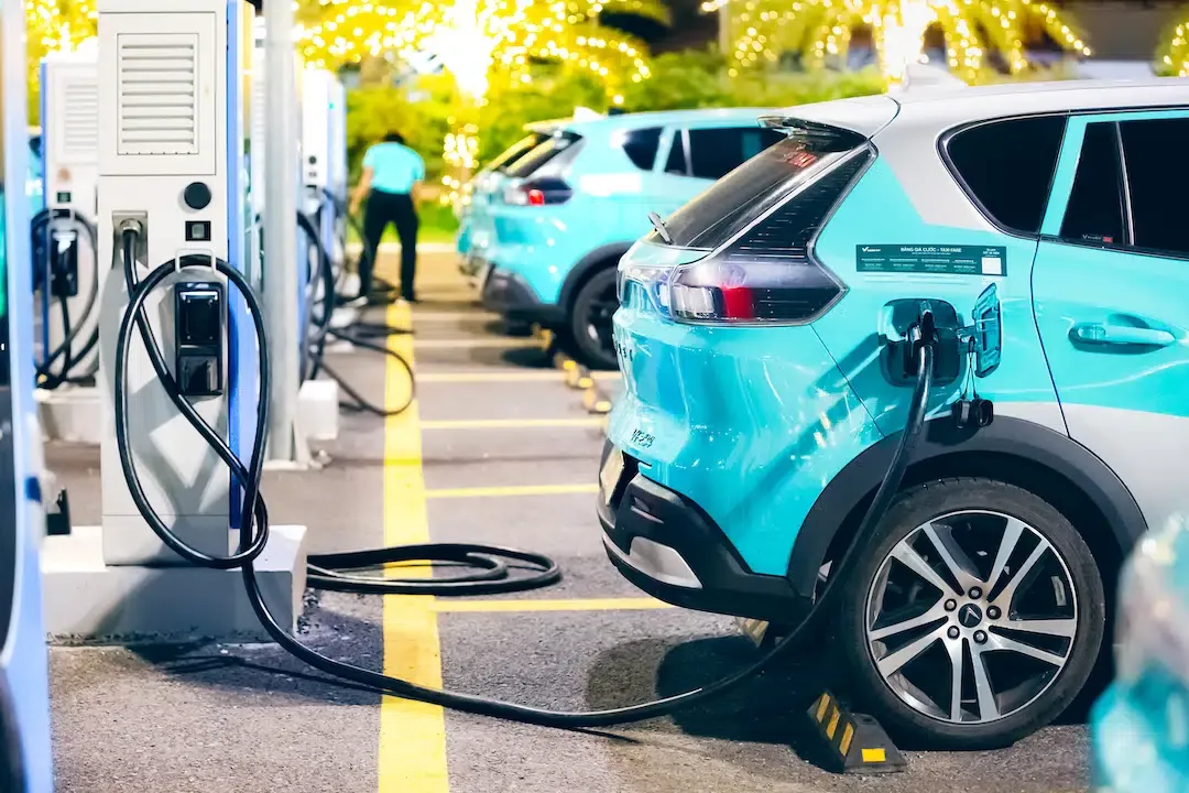 A fleet of light blue VinFast electric taxis charging at a station for eco friendly travel between Hue and Hoi An.