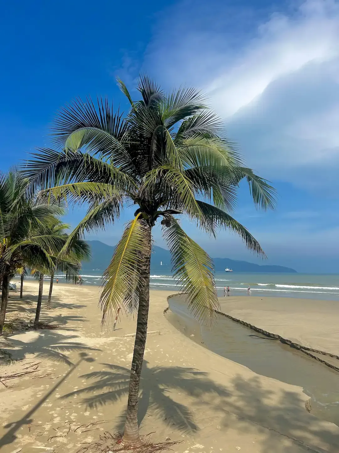 Scenic My Khe Beach in Da Nang featuring pristine white sand, turquoise seawater, and mountains in the distance with visitors swimming and sunbathing
