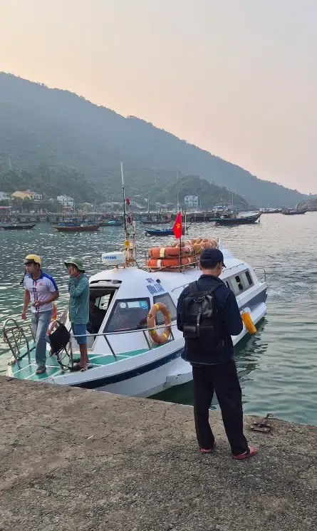 White speedboat docked at a stone pier for a transfer from Hoi An to Cham Island with green mountains in the background
