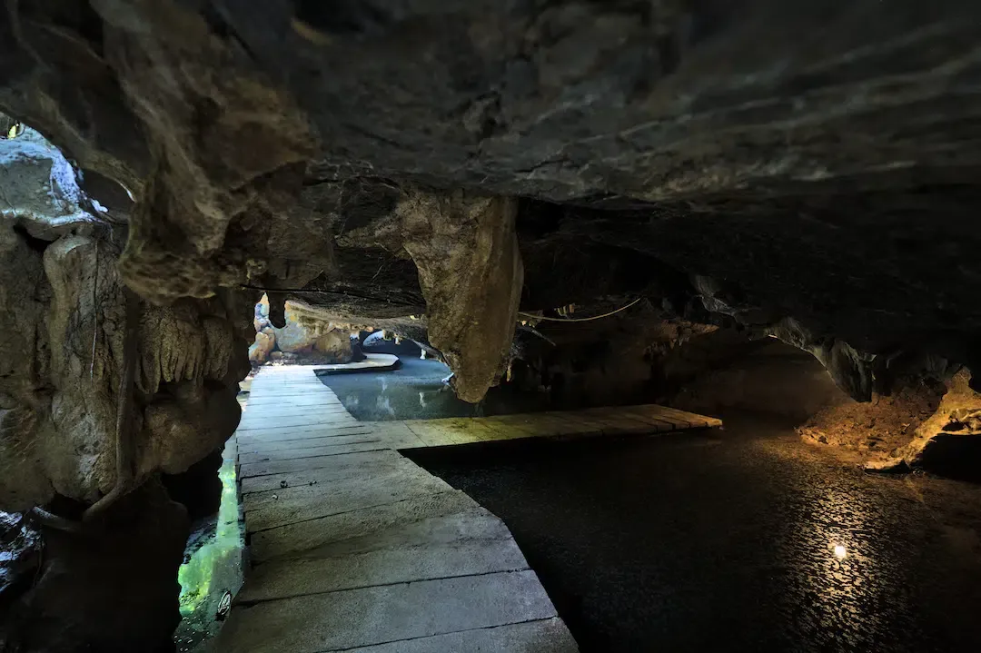 Wooden walkway over calm water inside the dark limestone But Cave at Thung Nham Bird Park.