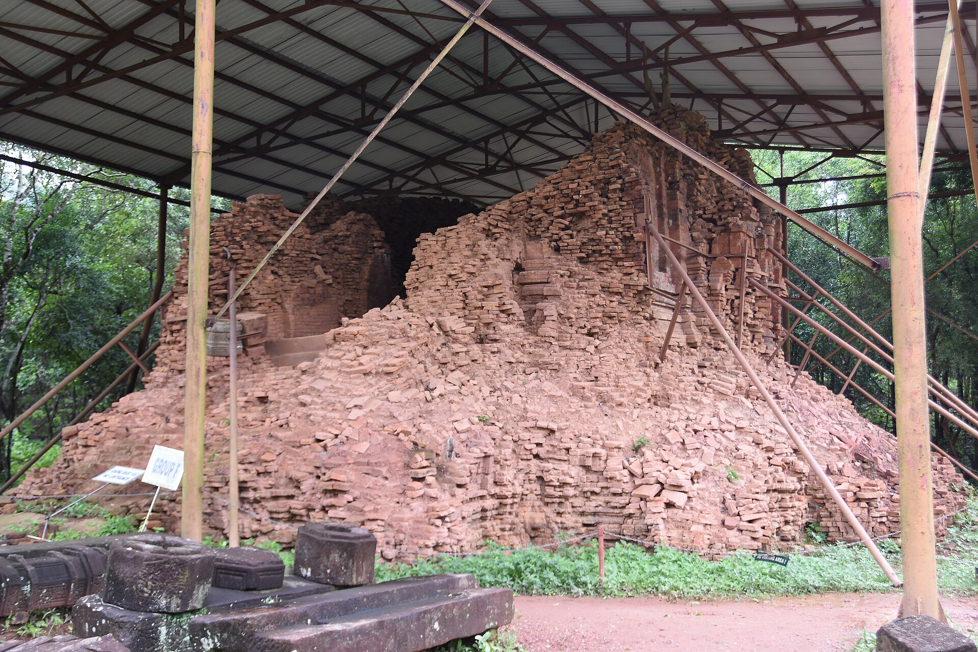 Collapsed brick tower at My Son held up by steel props under a metal roof