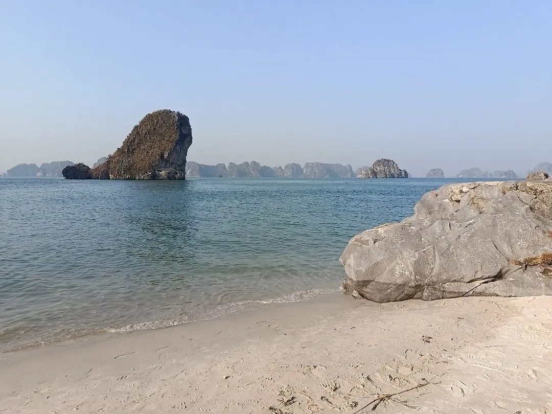 Pristine White Sand Beach at Bai Tu Long Bay With Large Limestone Boulder, Clear Turquoise Water, and Dramatic Limestone Island Formations in Background