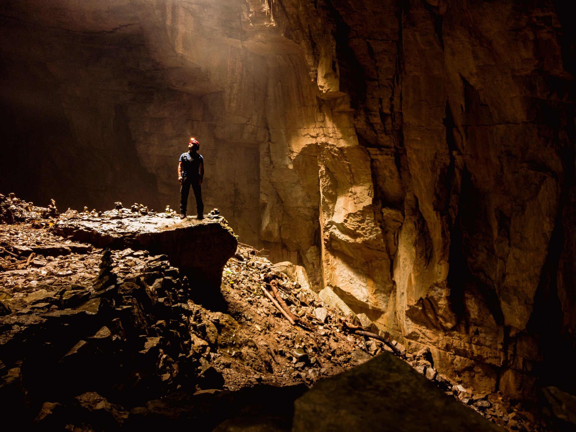 Person with a head torch standing on a rock ledge inside a large cave