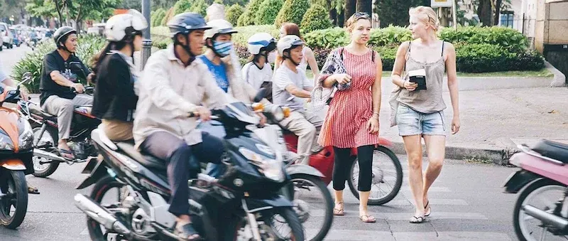 International tourists navigating the famous Vietnam motorbike traffic while crossing a busy city street in Hanoi or Ho Chi Minh City.