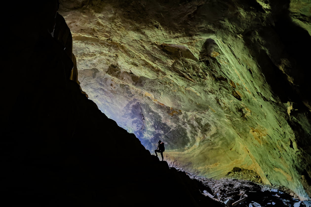A hiker standing in the green-lit mouth of Hang Pygmy cave looking up at the walls