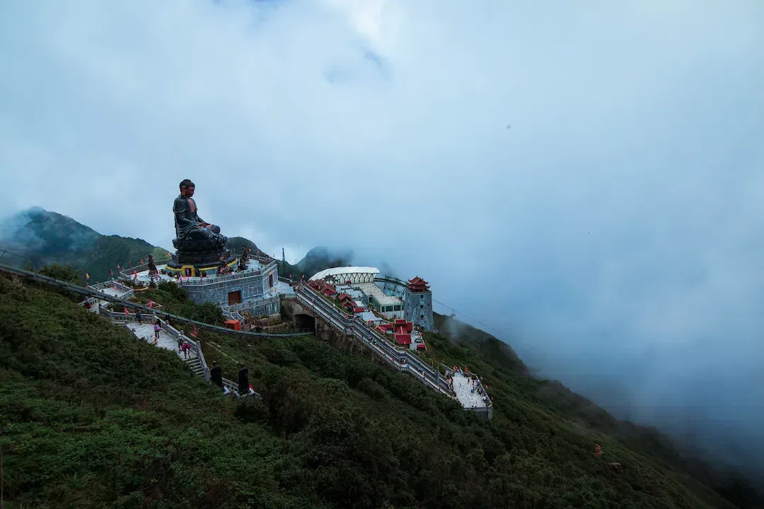 Large bronze Buddha statue at the Fansipan mountain peak in Sapa Vietnam with clouds and stone walkways
