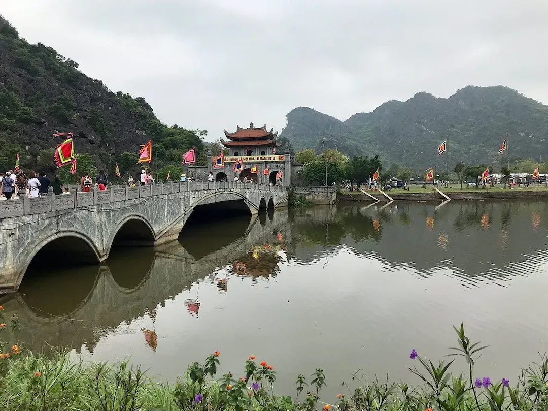 Hoa Lu Ancient Capital Stone Bridge With Traditional Pagoda Temple and Limestone Mountains in Ninh Binh Vietnam During Truong Yen Festival Celebration With Red Flags
