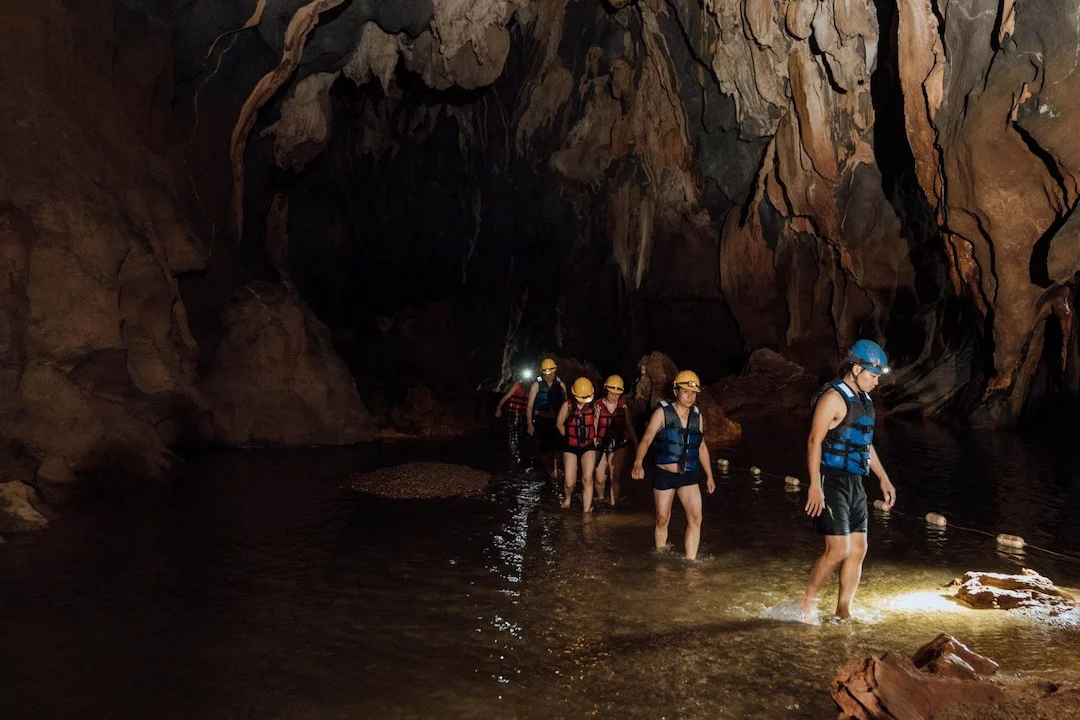 Visitors covered in grey mud floating in the mud pool inside Dark Cave