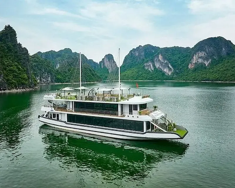 A luxury white cruise boat sailing through the emerald green water and iconic limestone karsts of Ha Long Bay, Vietnam