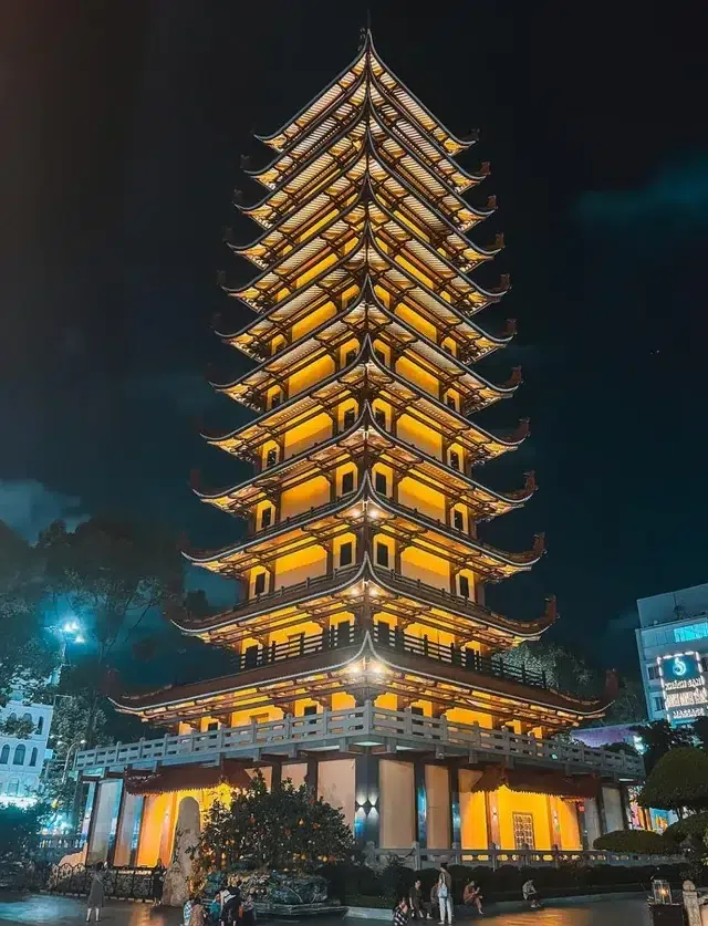 The tall 13-story illuminated stupa of Vietnam Quoc Tu Pagoda in Ho Chi Minh City at night with glowing yellow lights and traditional tiered roofs.