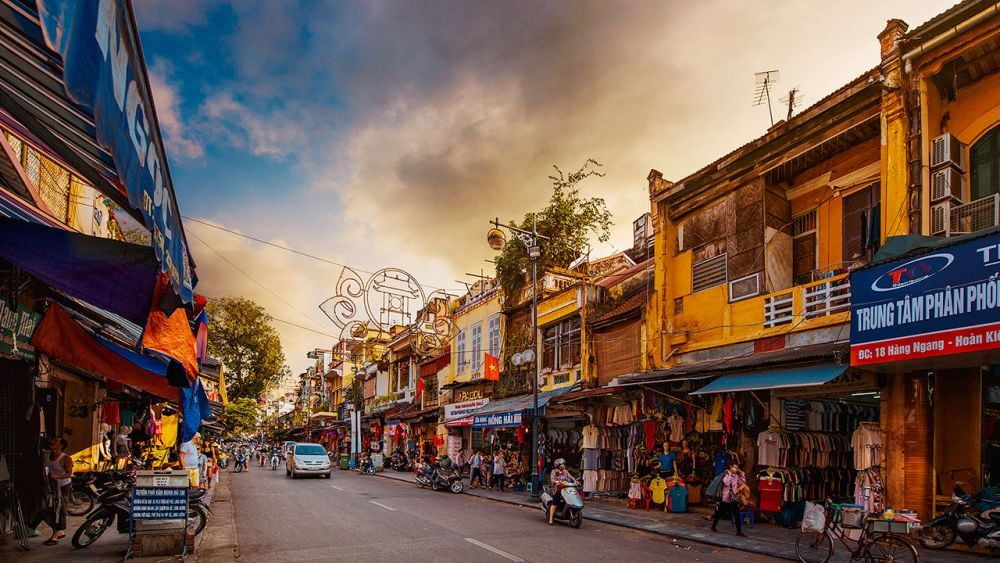 3. Street View of Hanoi S Old Quarter in Vietnam, Featuring Bustling Shops, Motorbikes, and Traditional Yellow Colonial Buildings Under a Vibrant Evening Sky