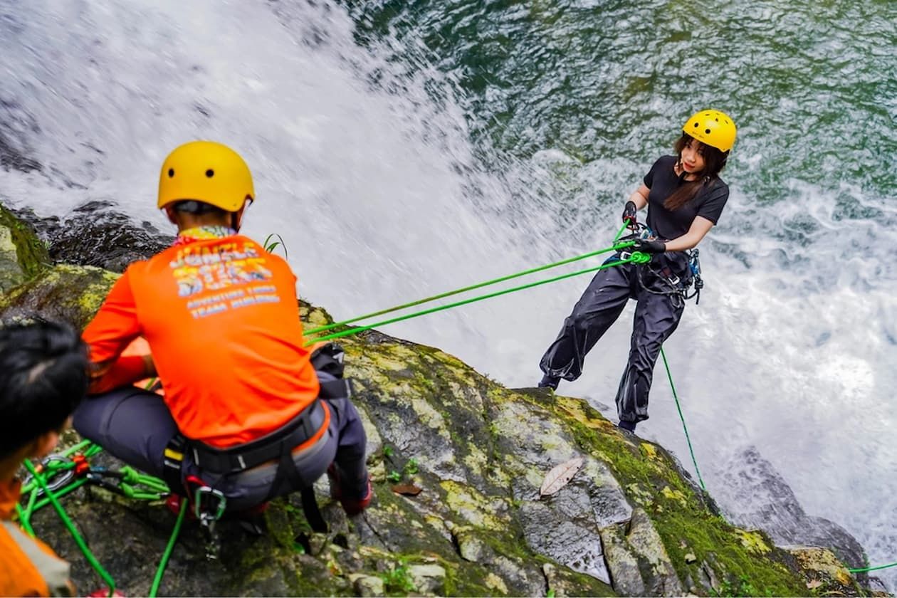 Hiker Doing Waterfall Rappelling While Jungle Boss Safety Staff Secure Her in Foreground