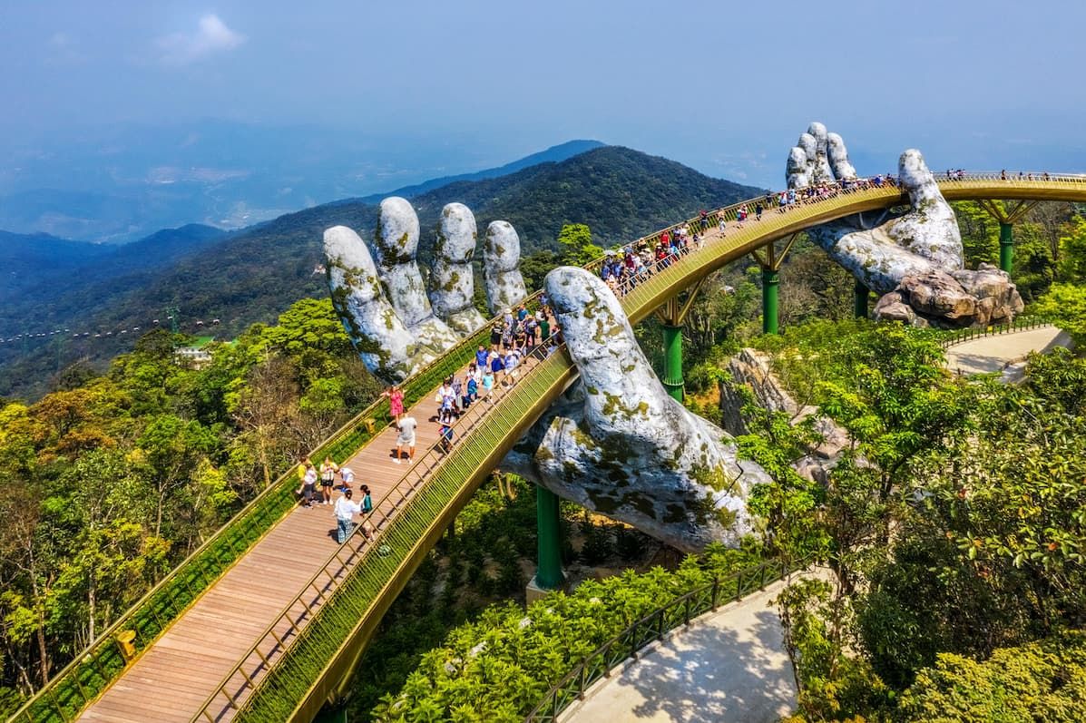2. Aerial View of the Golden Bridge in Da Nang, Vietnam, Featuring a Pedestrian Walkway Supported by Two Giant Stone Hands Surrounded by Lush Green Mountains and Forest