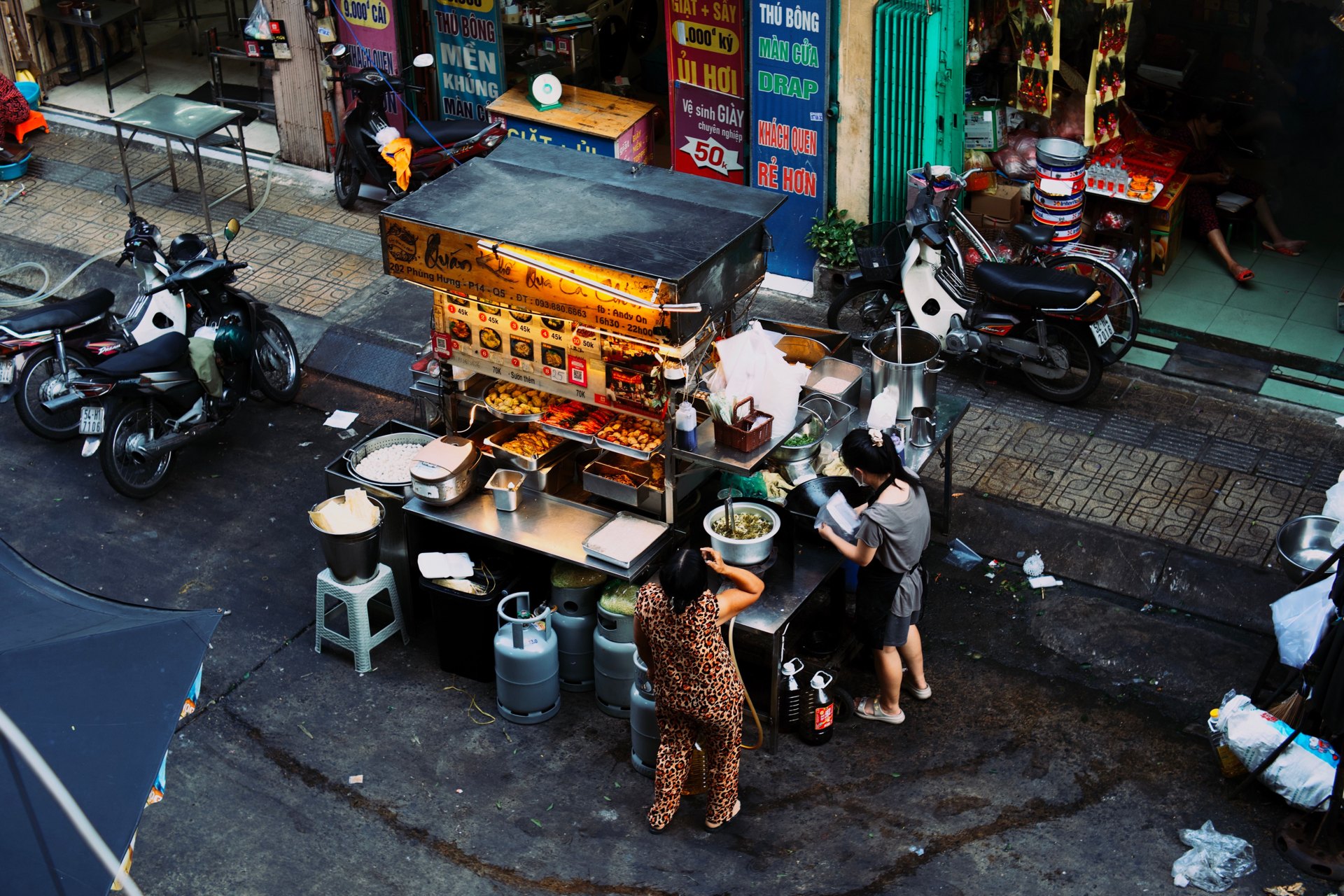 Two women cooking at a street food cart in Vietnam, seen from above