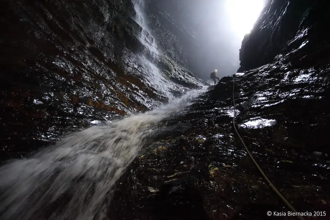 A caver rappelling down a massive wet rock face next to a roaring subterranean waterfall in Sistema Huautla Mexico