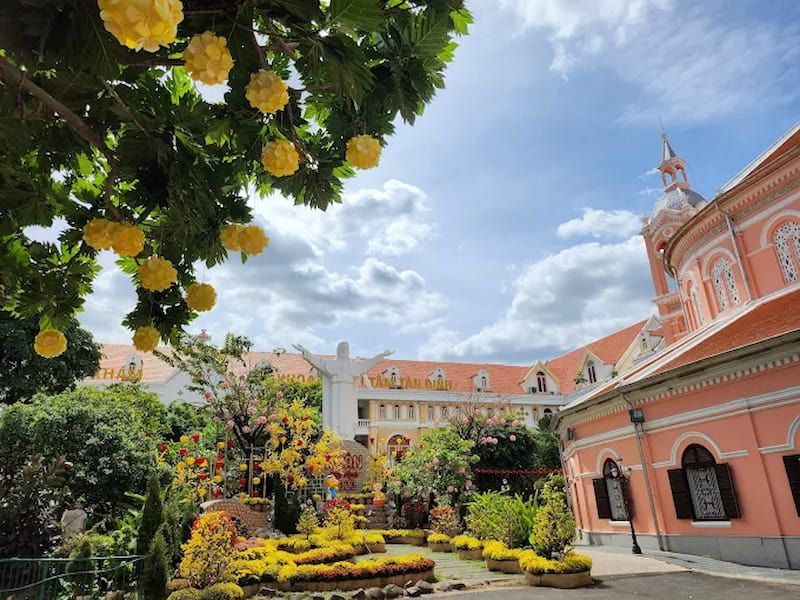 Tan Dinh Church courtyard garden with yellow flowers, white crucifix statue, and pink church exterior in Ho Chi Minh City