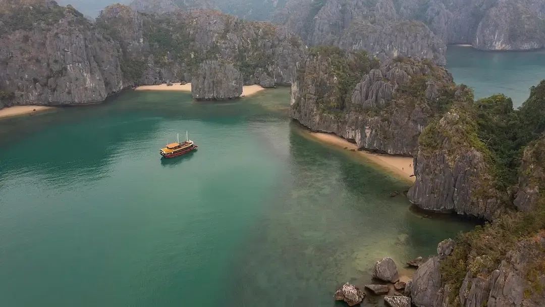 Aerial View of Secluded Cove in Lan Ha Bay With Sandy Beaches Limestone Cliffs and a Single Wooden Junk Boat