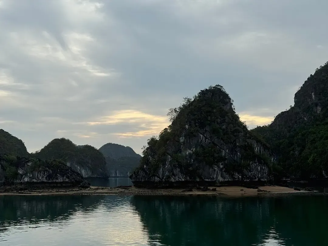 Calm Lagoon in Lan Ha Bay With Limestone Islands Reflected in Still Green Water Under Cloudy Evening Sky
