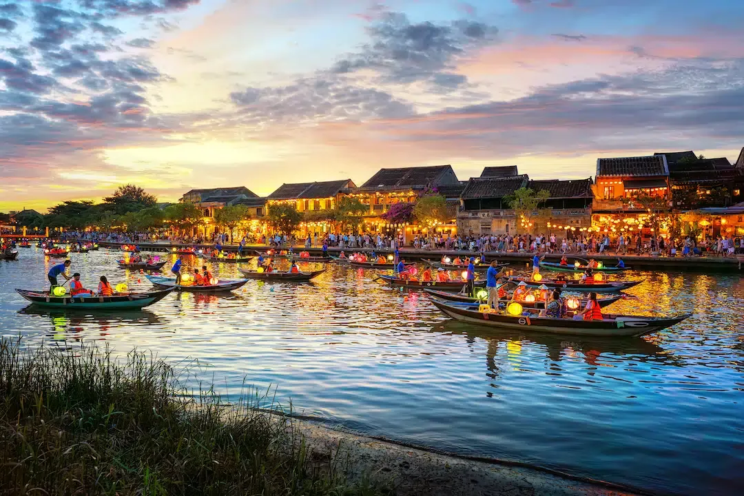 Colorful lanterns reflecting on the river in Hoi An Ancient Town with traditional wooden boats at sunset.