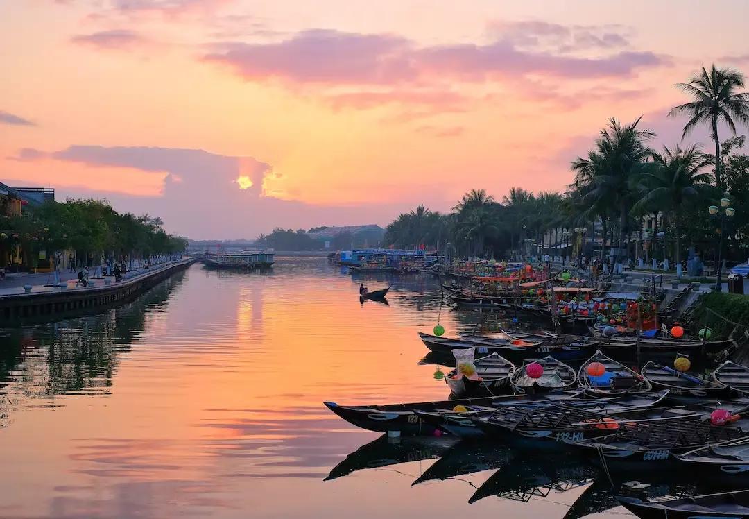Traditional wooden boats docked on Thu Bon River in Hoi An during a pink and orange sunset