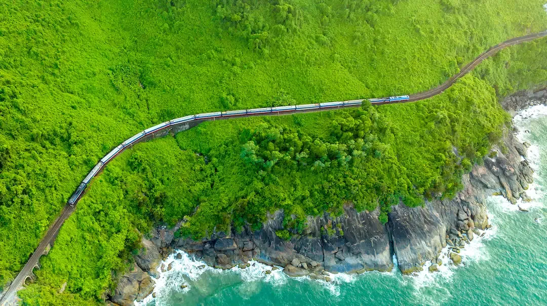 Aerial view of the Reunification Express train winding along the scenic coastline of the Hai Van Pass between Hue and Da Nang.