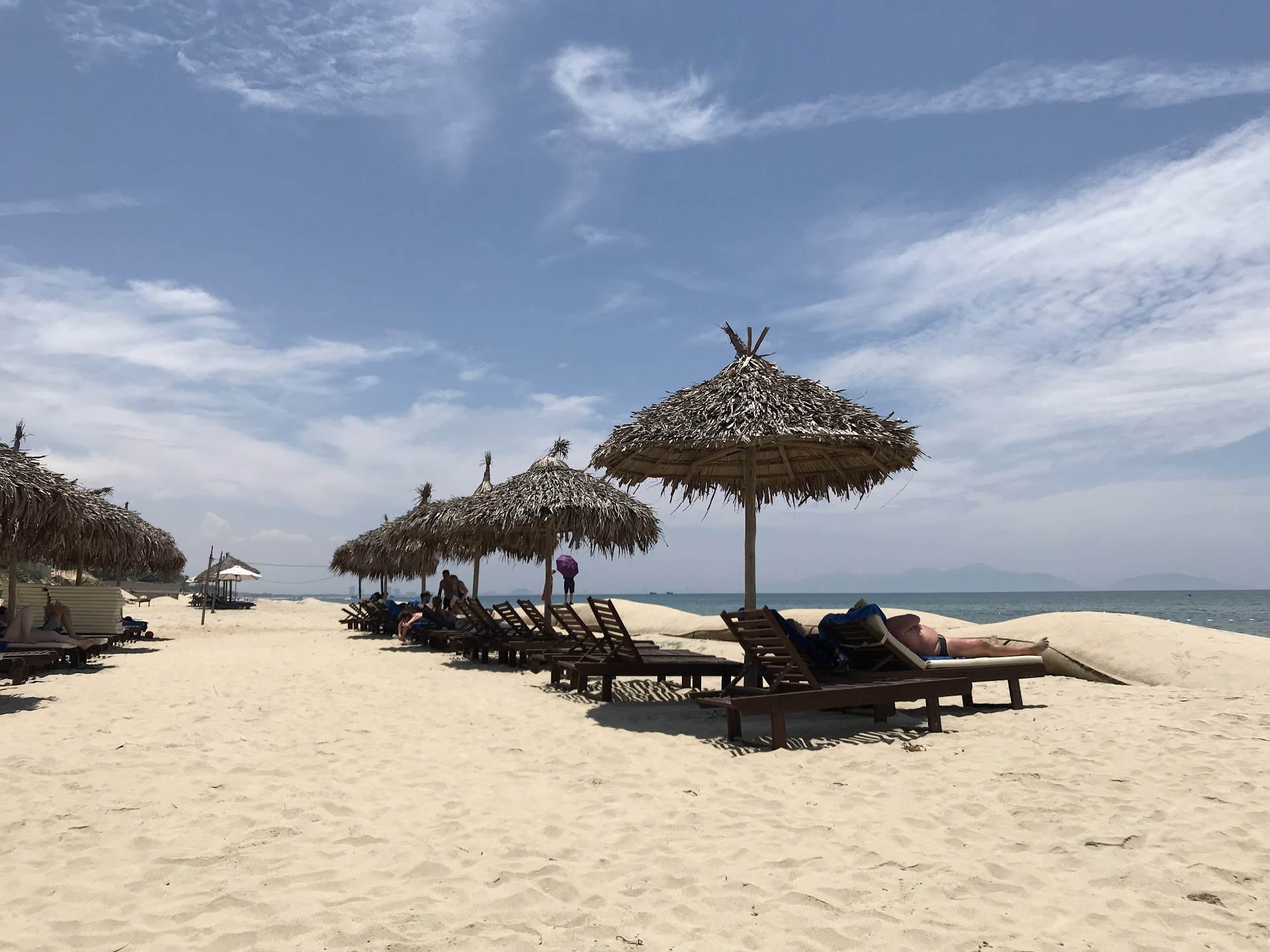 Thatched umbrellas and wooden sun loungers on the sand at An Bang beach