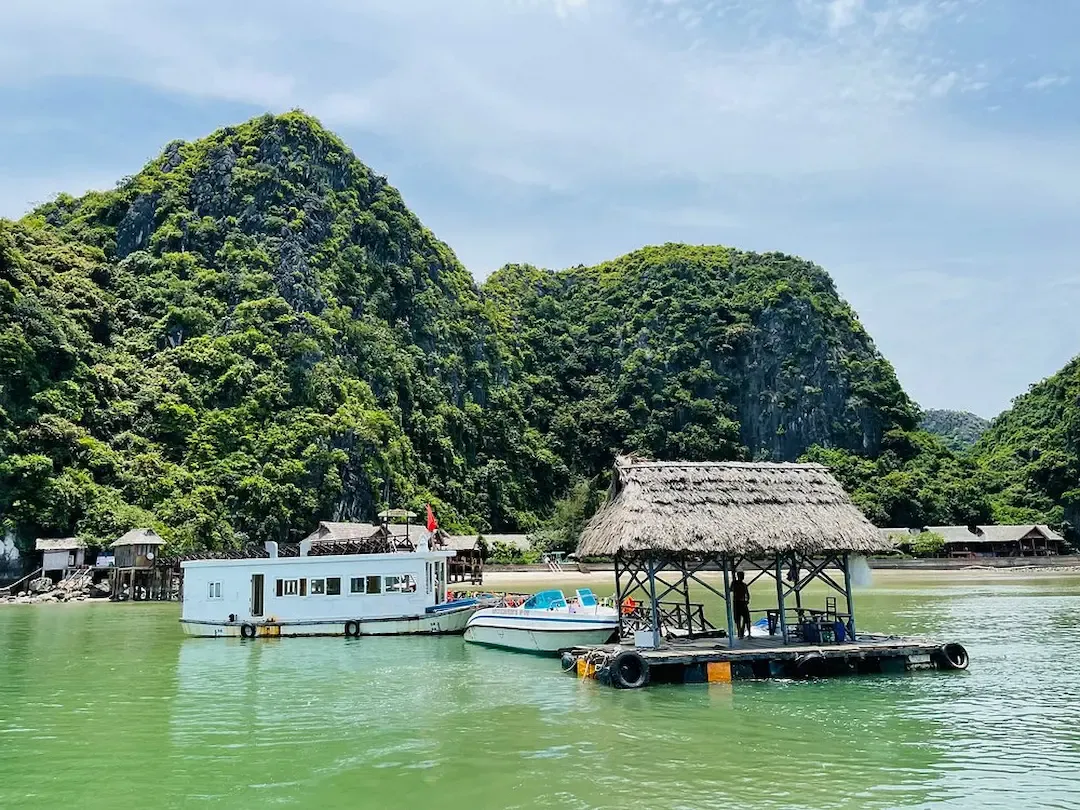 Floating Wooden Platform and Boats Anchored Below Lush Green Limestone Hills in Lan Ha Bay Vietnam