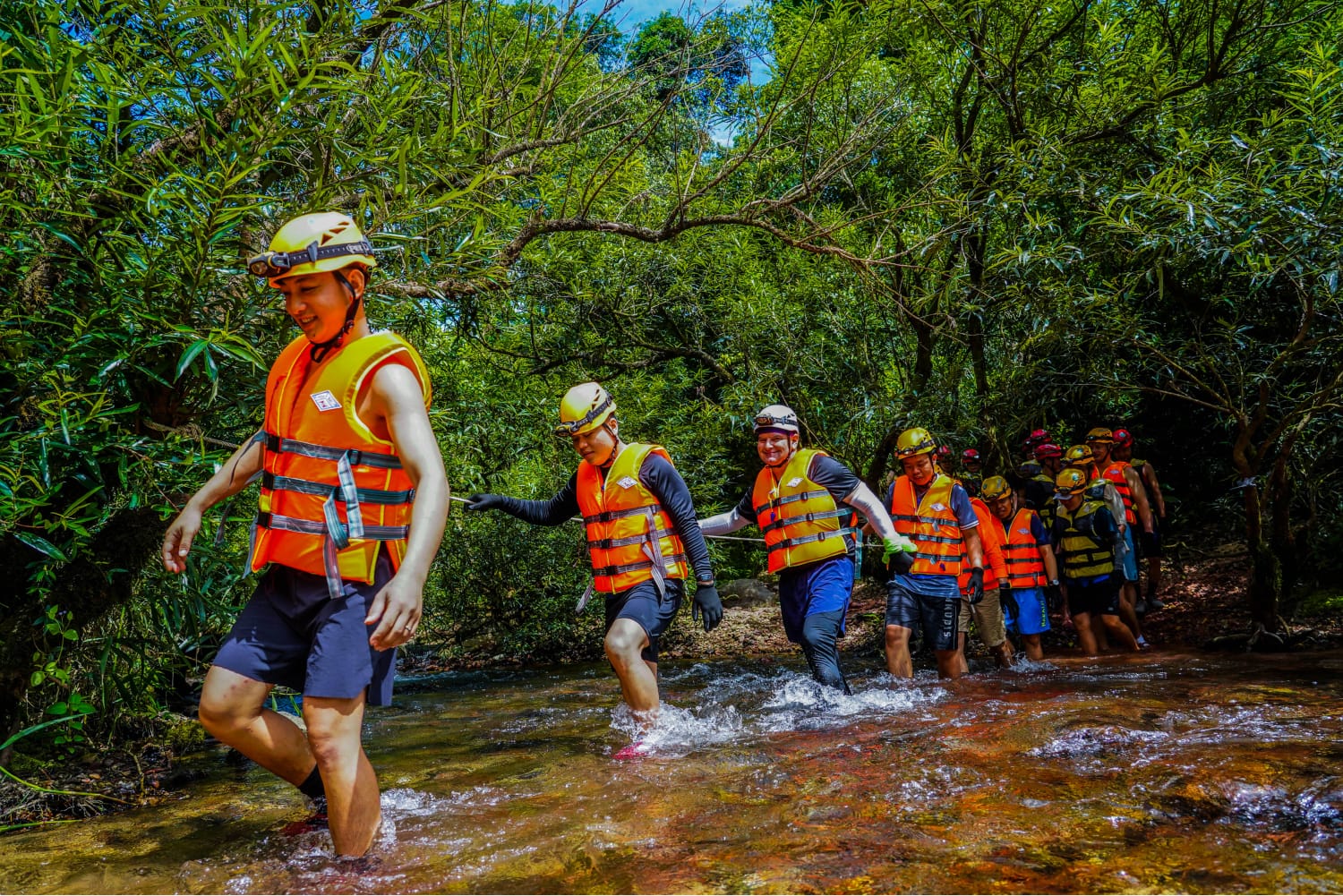 Trekker crossing a knee-deep stream on slick rock with an arm out for balance