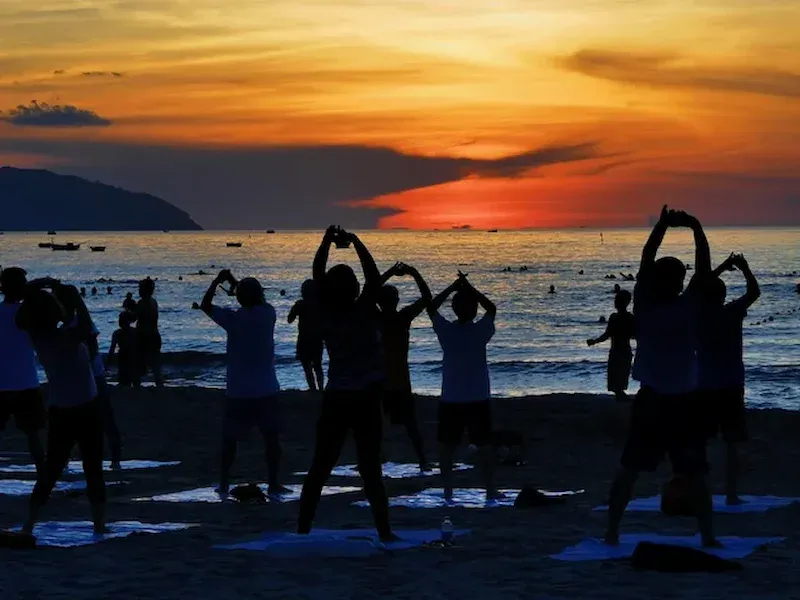 My Khe Beach during golden hour sunset with silhouettes of people making heart shapes, calm sea reflecting orange sky, and palm trees
