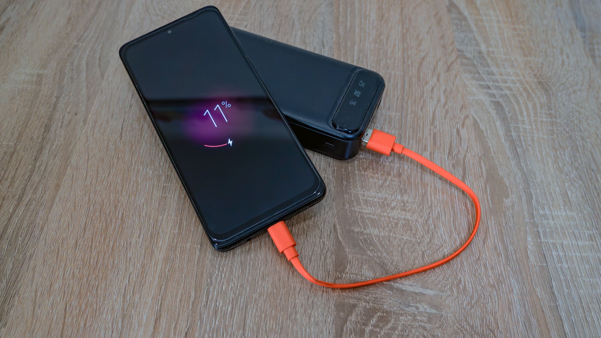 Phone at 11 percent charging from a black power bank with an orange cable