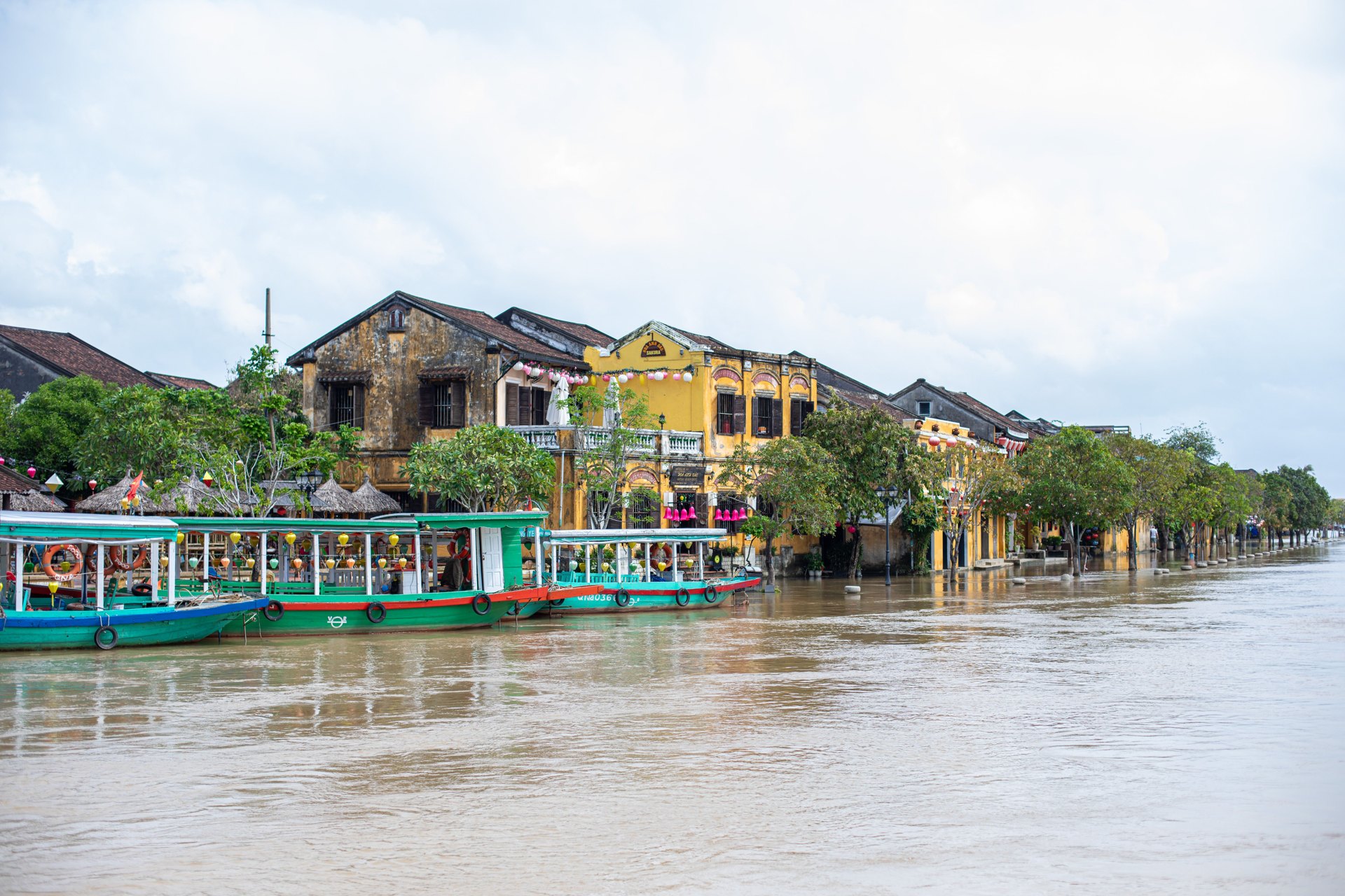 Brown floodwater level with the riverfront houses and tour boats in Hoi An
