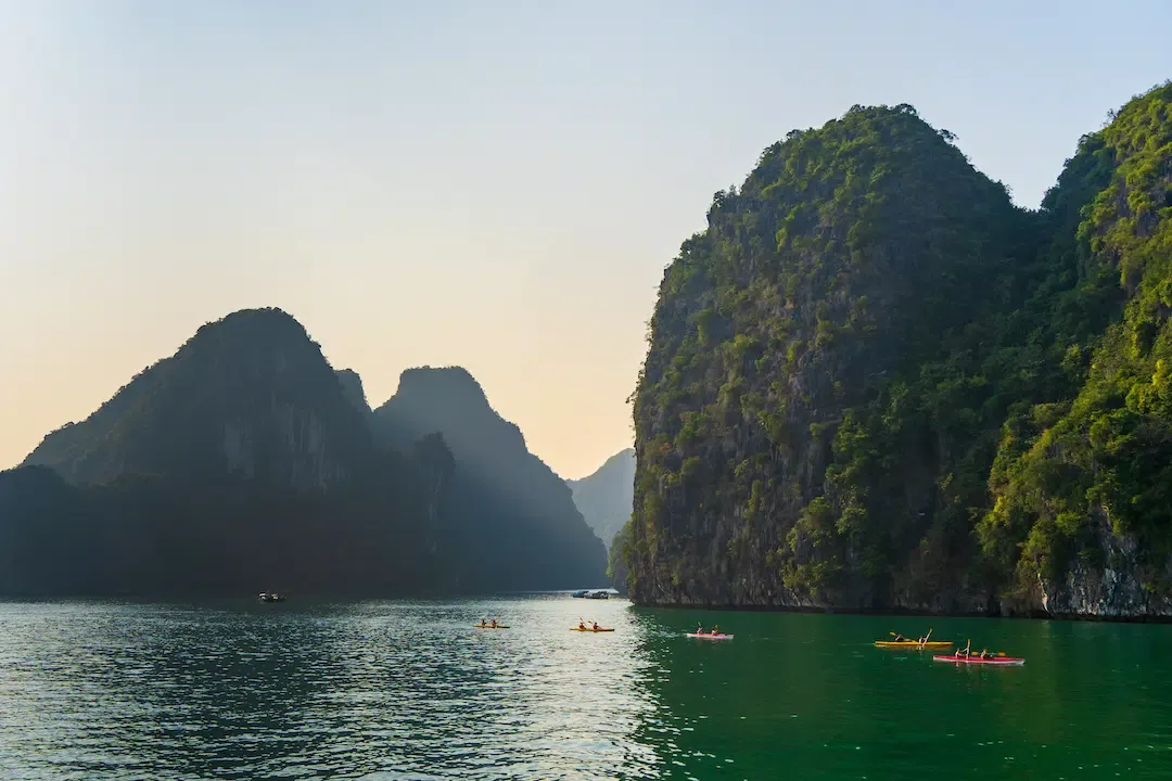 Small group of travelers on a kayaking excursion along towering jungle covered karst cliffs in Lan Ha Bay.