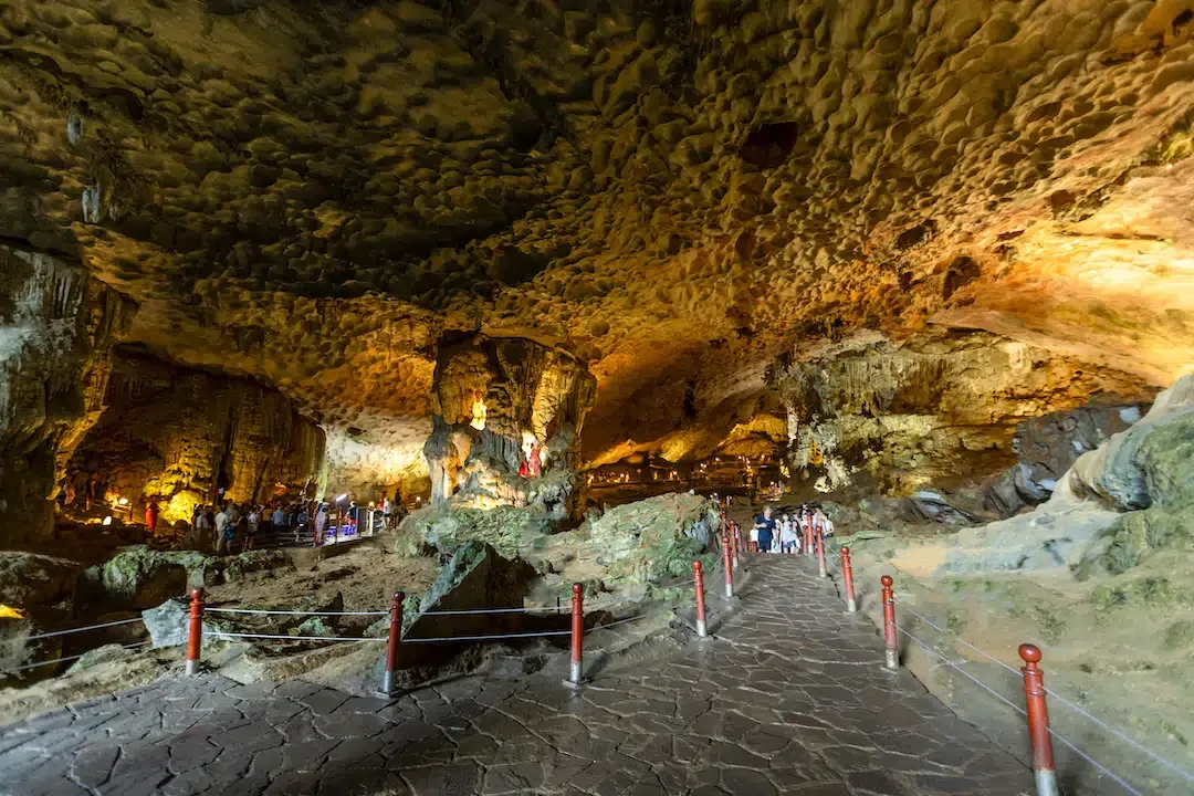 Interior view of Sung Sot Cave in Ha Long Bay featuring a paved stone walkway with red railings surrounded by massive limestone pillars and a textured ceiling