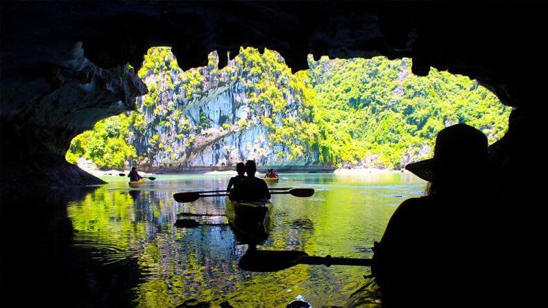 Silhouettes of Kayakers Exploring Dark and Bright Cave With Lush Landscape Visible Through the Cave Entrance.