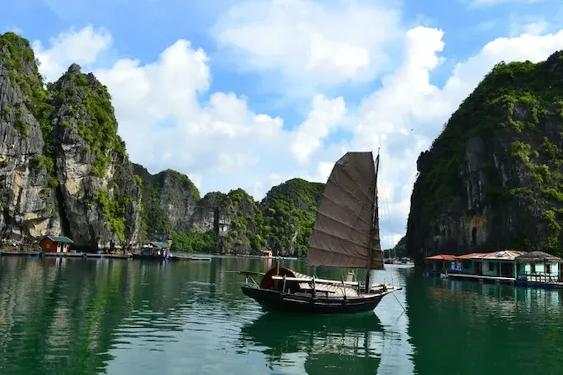 Traditional wooden junk boat with dark sail in Vung Vieng fishing village, Bai Tu Long Bay, Vietnam