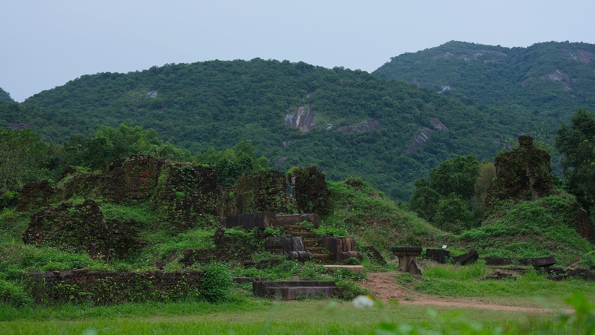 Grass-covered ruins of temple group A at the foot of forested hills at My Son