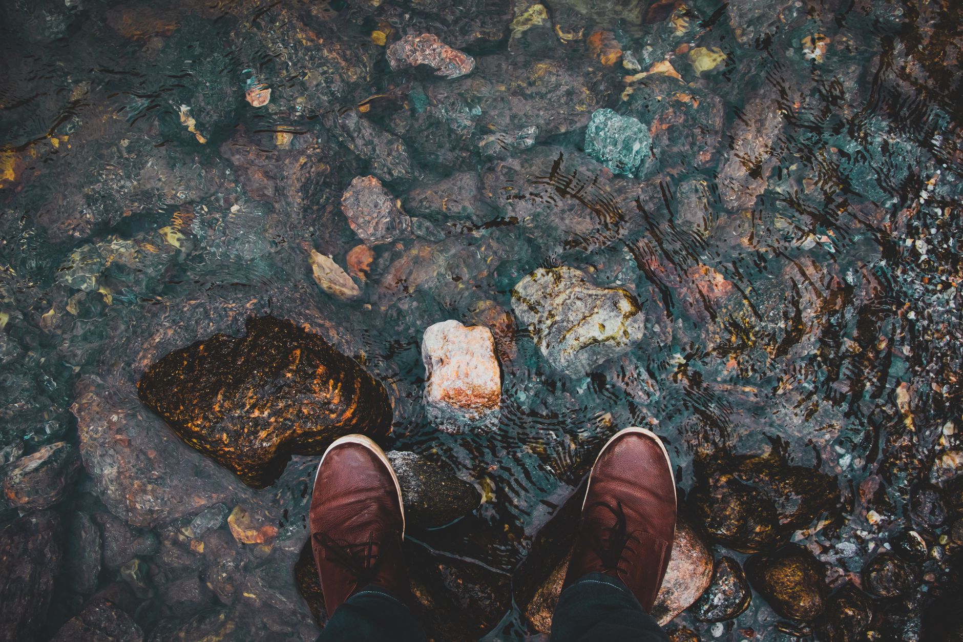 Soaked canvas trekking shoes draining on a rock beside a stream