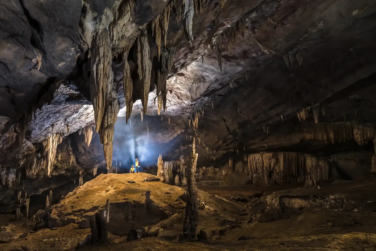 Enormous stalactite formations and cave explorers during a technical caving tour in Vietnam.