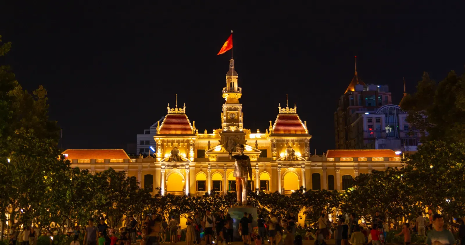 The illuminated Ho Chi Minh City People's Committee Building and the Ho Chi Minh statue at night in District 1.