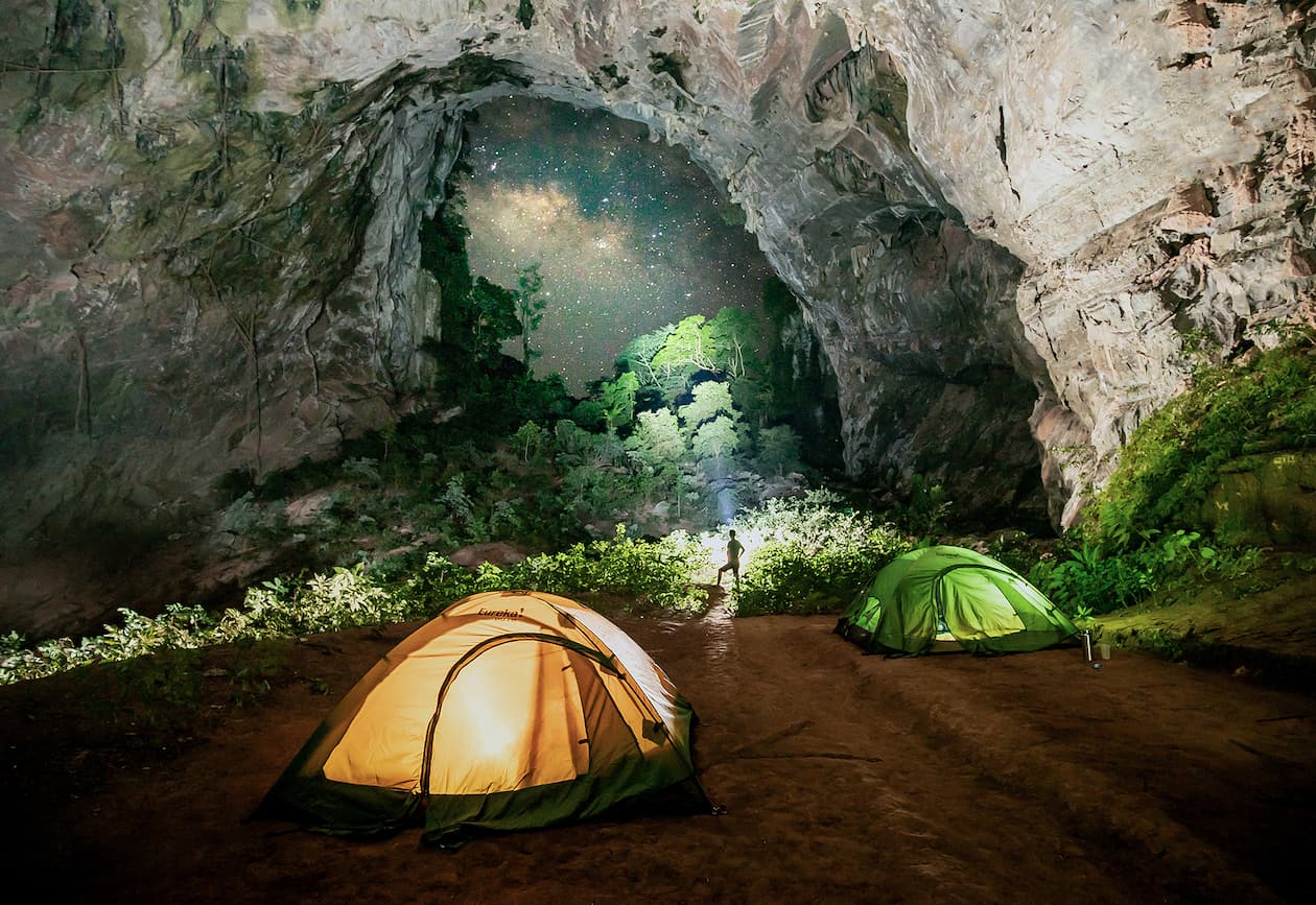 Tents pitched inside a cave doline with jungle visible through the opening