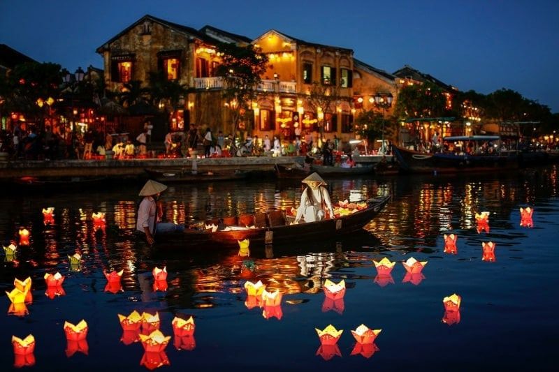 Lanterns Floating on the River in Hoi An, Vietnam, With People in Boats and Illuminated Buildings in the Background