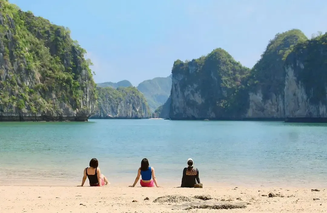 A Pristine White Sand Beach in Lan Ha Bay Area With Turquoise Waters, Tourists Swimmingrelaxing, and Dramatic Limestone Karst Cliffs Forming the Backdrop.