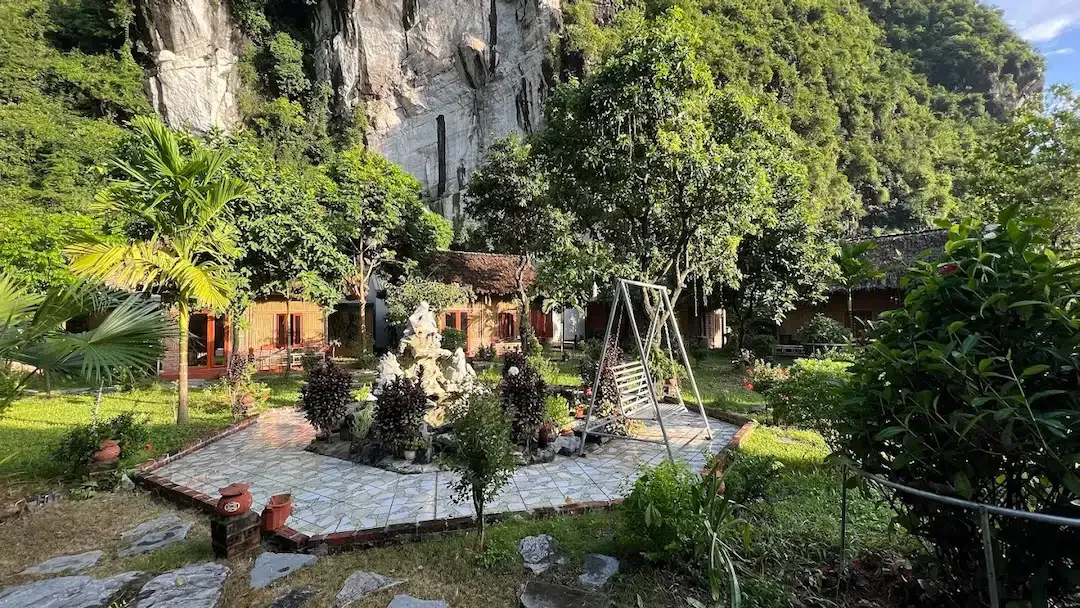 Lush garden courtyard with traditional bungalow rooms built at the base of a dramatic limestone cliff face at Trang An River View Homestay in Ninh Binh Vietnam