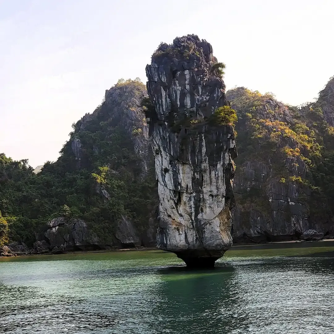 Tall Limestone Karst Tower Rising From Emerald Green Water in Lan Ha Bay Vietnam