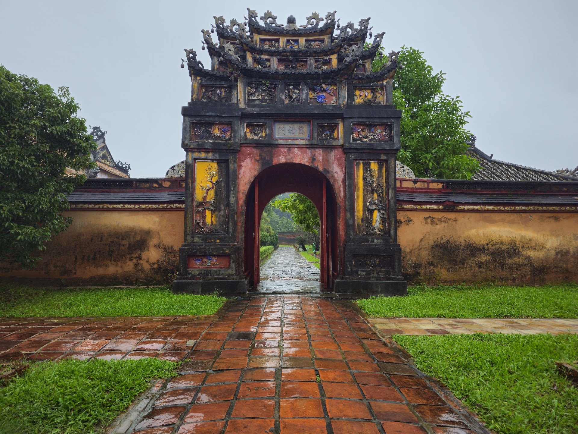Ornate gate in the Hue Imperial City with wet brick paving under a grey sky