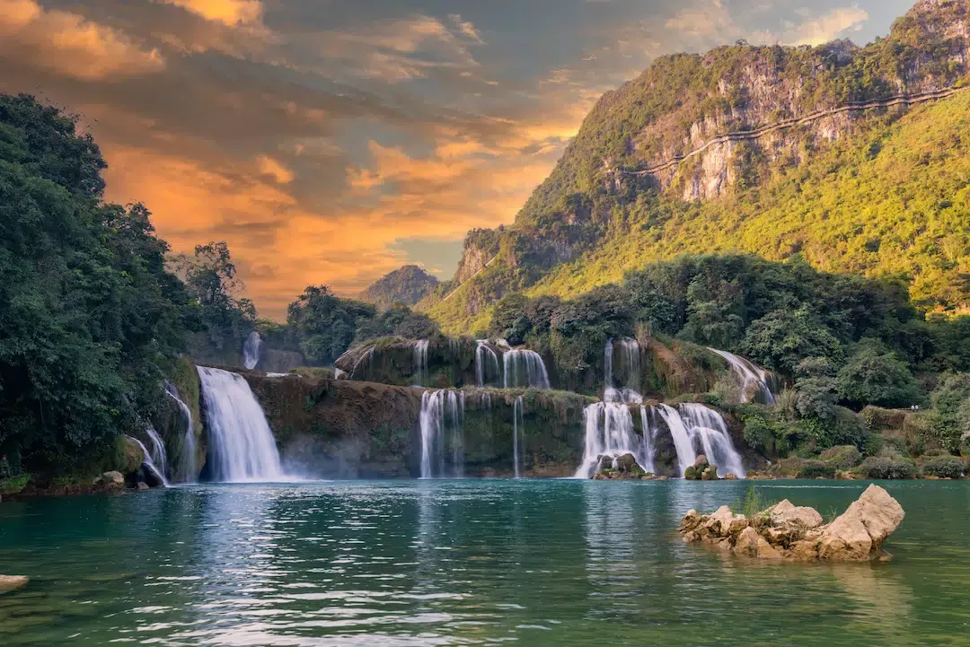 The majestic Ban Gioc Waterfall with multiple tiers of white water falling into a turquoise river on the border of Vietnam and China