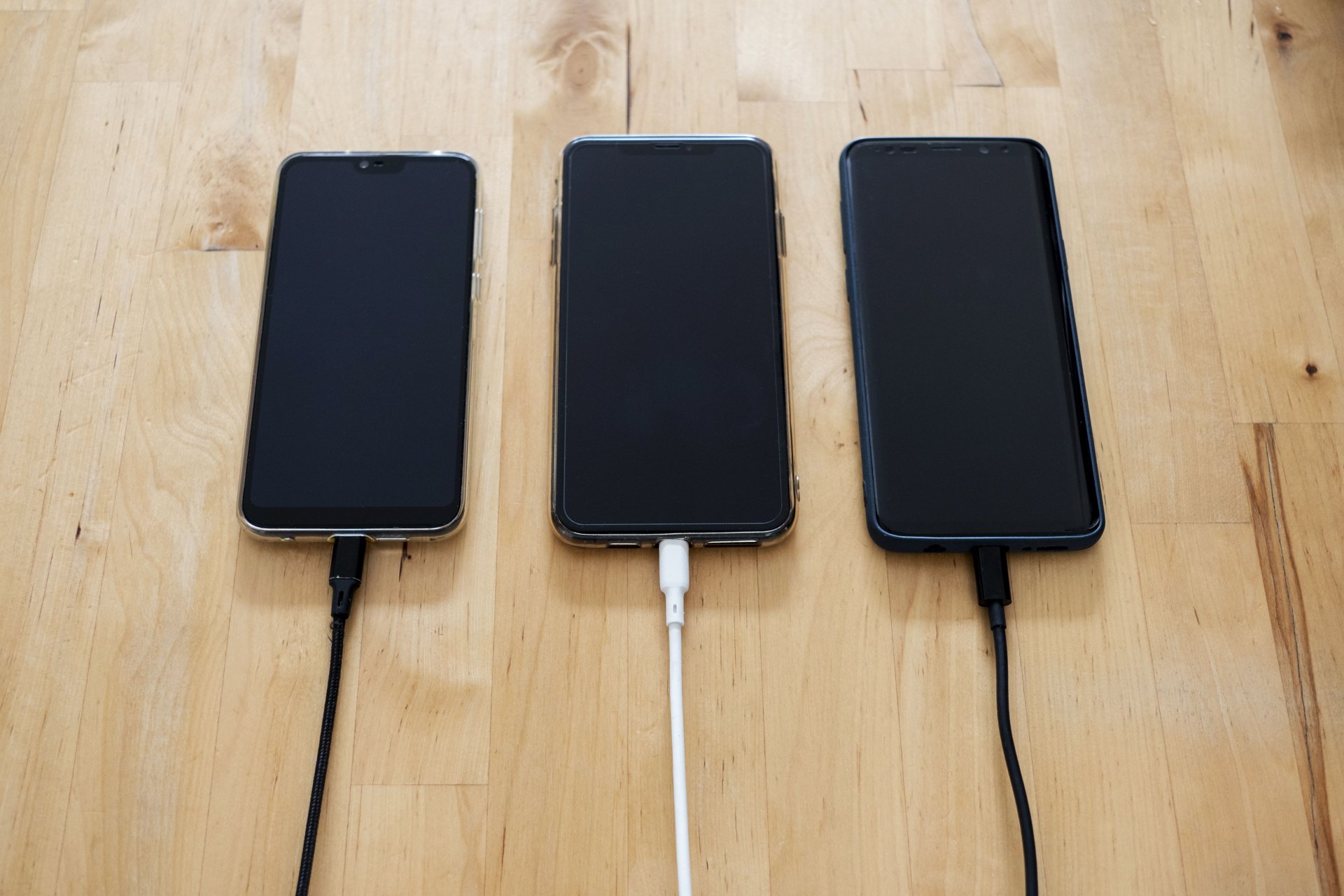 Three phones charging side by side on a wooden table
