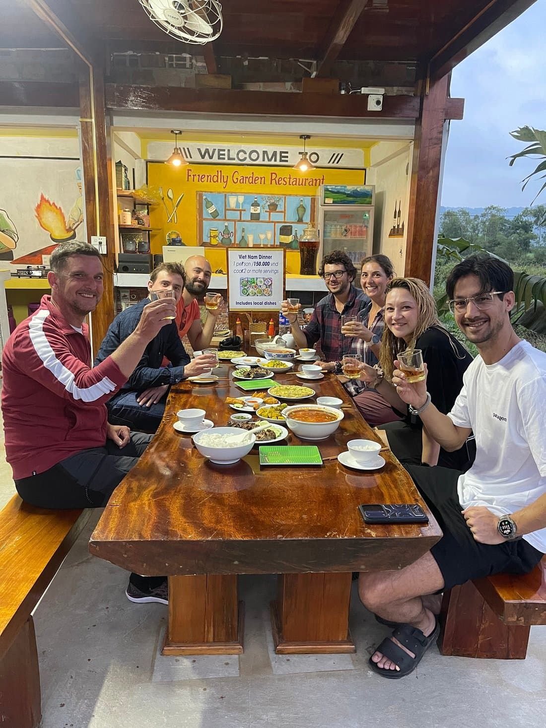 Group of Friends Enjoying a Vietnamese Dinner at Friendly Garden Restaurant, Sitting Around a Wooden Table With Various Local Dishes