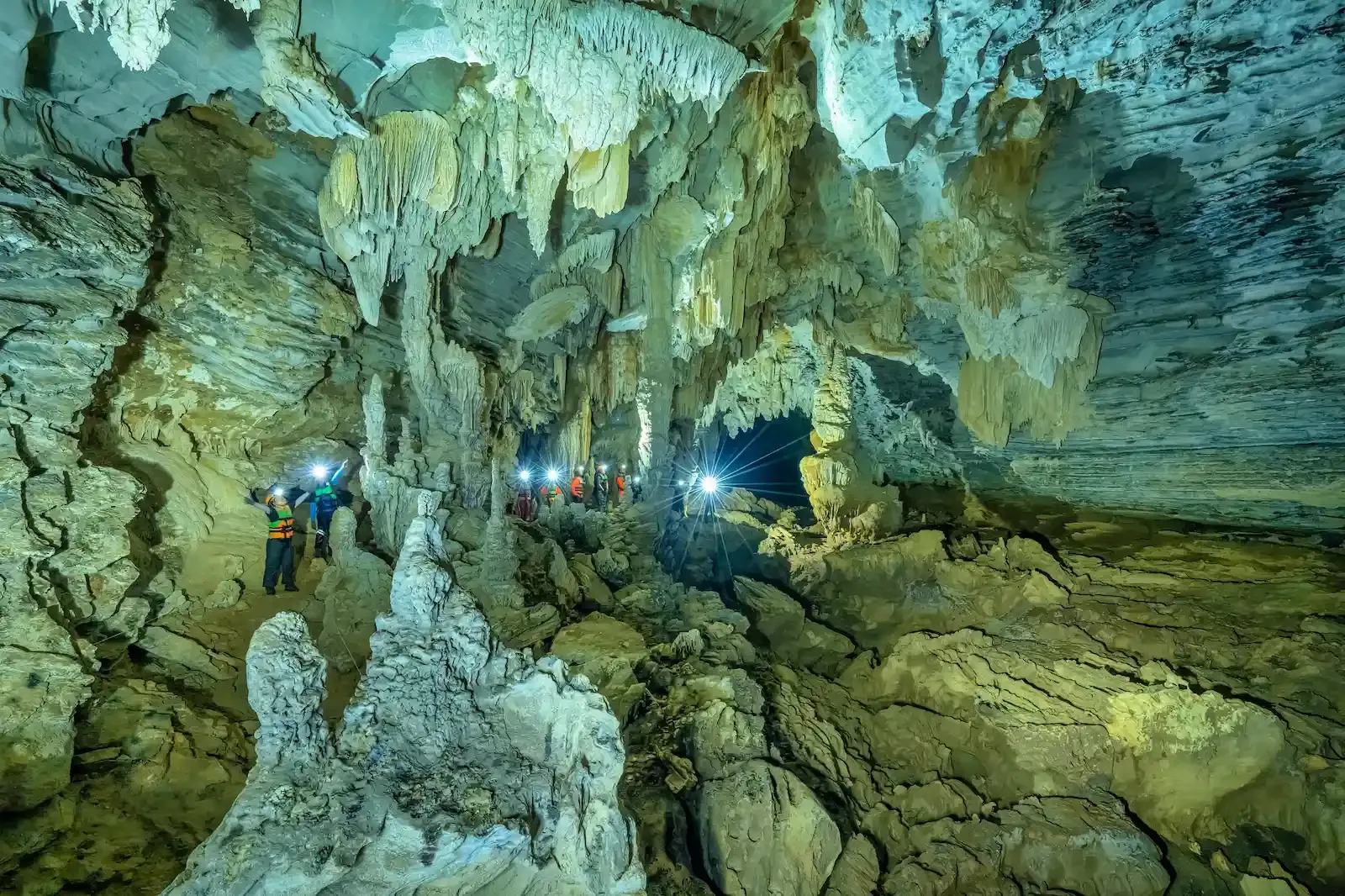 Cavers scrambling over boulders toward the jungle-lit entrance of the Tu Lan Cave System on the Tu Lan Cave Expedition in Vietnam