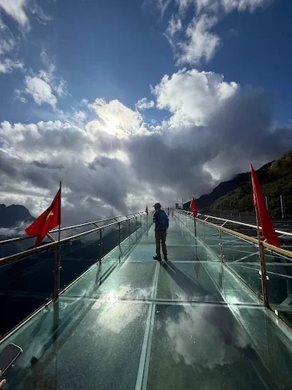 Tourist on the Glass Walkway bridge of Rong May (sapa, Vietnam) With Vietnamese Flags and a Dramatic Cloud Filled Mountain Sky